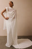 A model wearing a flowing white draped gown with a high draped neckline and a long train, standing against a warm beige wall.