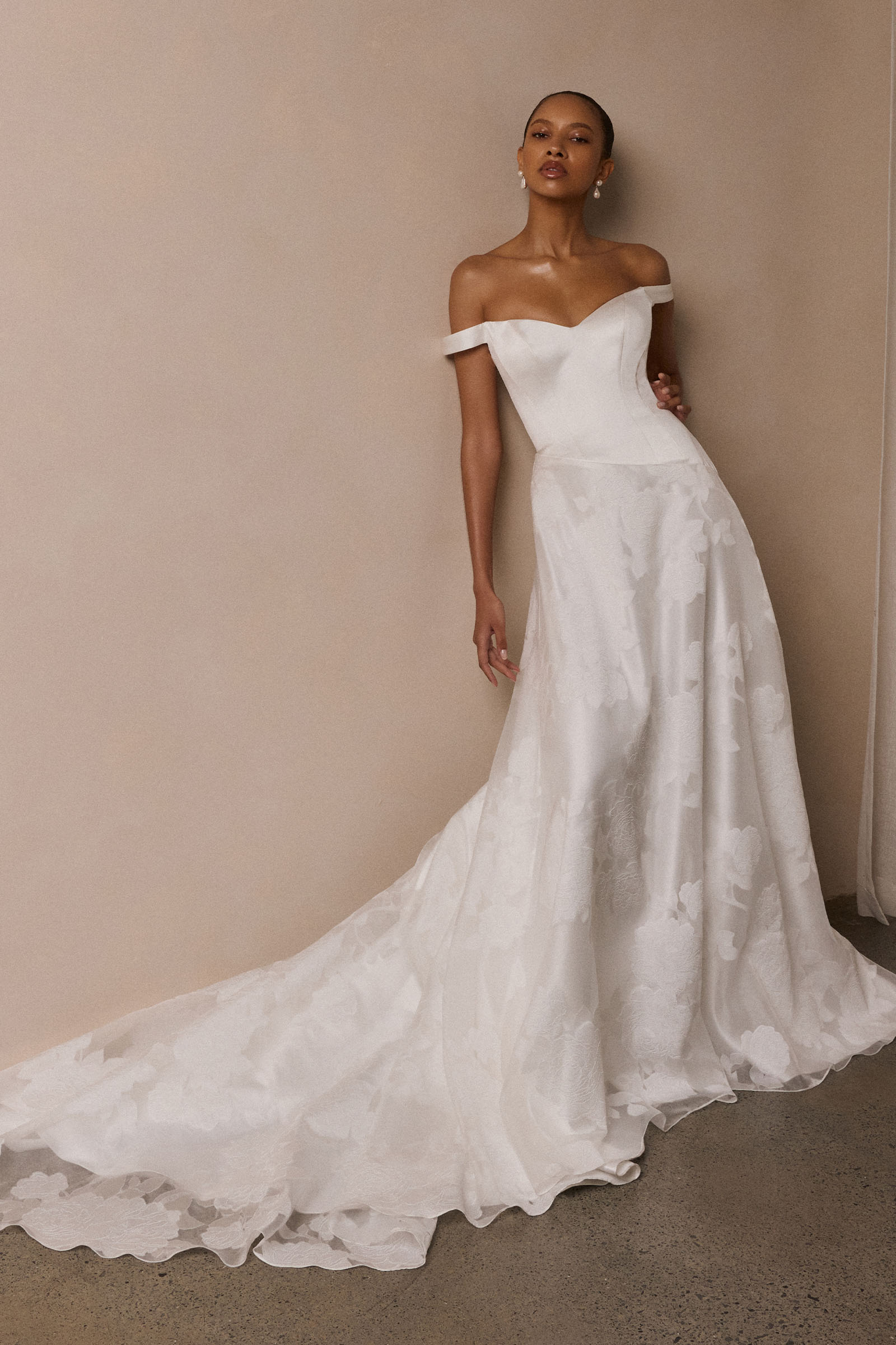 A woman wearing an off-the-shoulder white wedding dress with a fitted bodice and flowing skirt_XS_