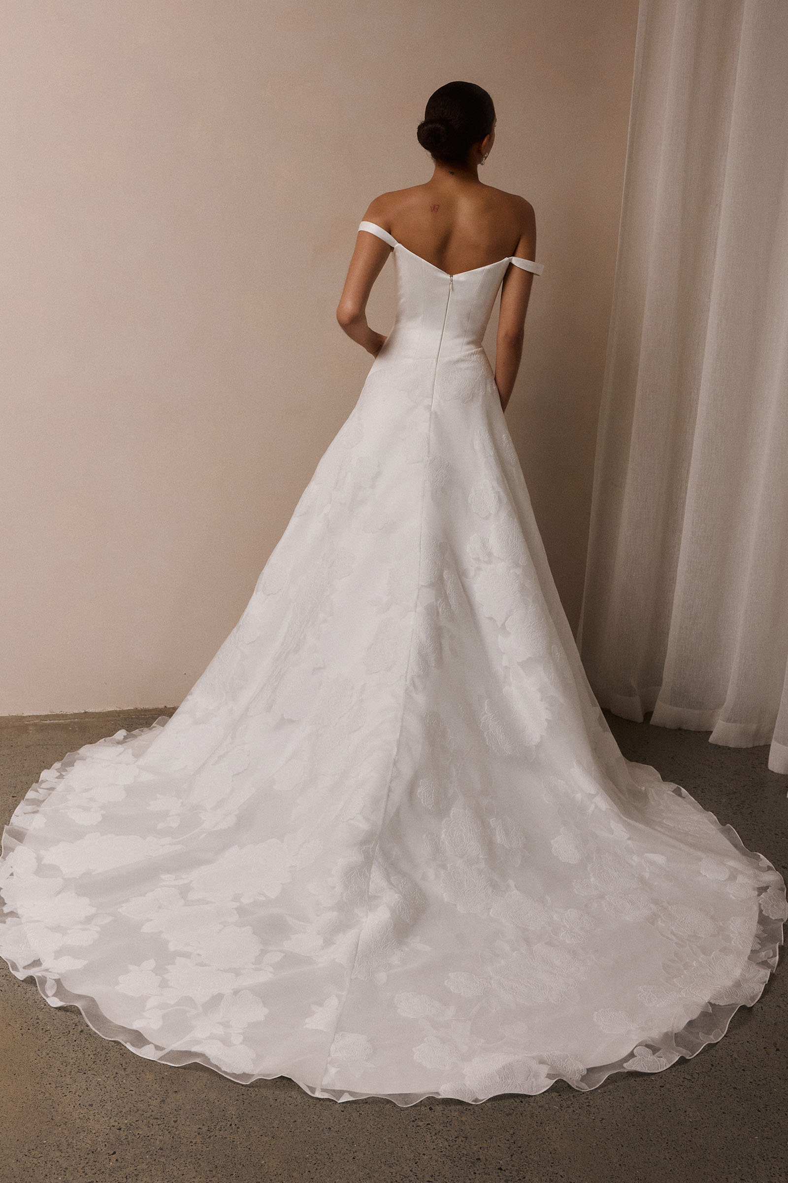 A woman wearing an off-the-shoulder white wedding dress with a fitted bodice and flowing skirt_XS_