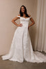 A woman wearing an off-the-shoulder white wedding dress with a fitted bodice and flowing skirt_L_