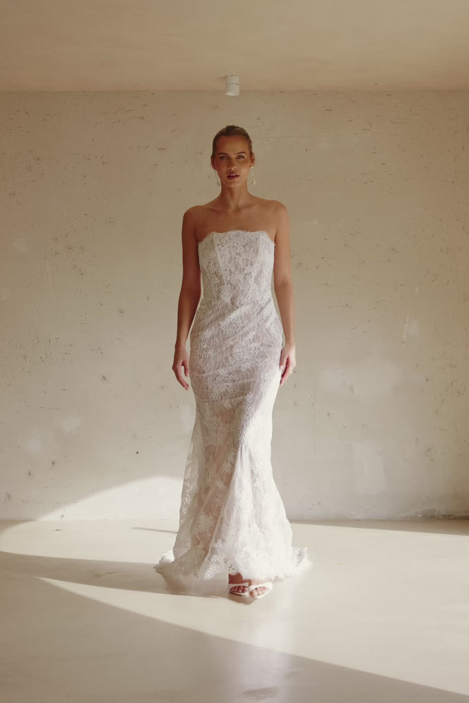 Video of a woman wearing a strapless white lace wedding gown with a long train