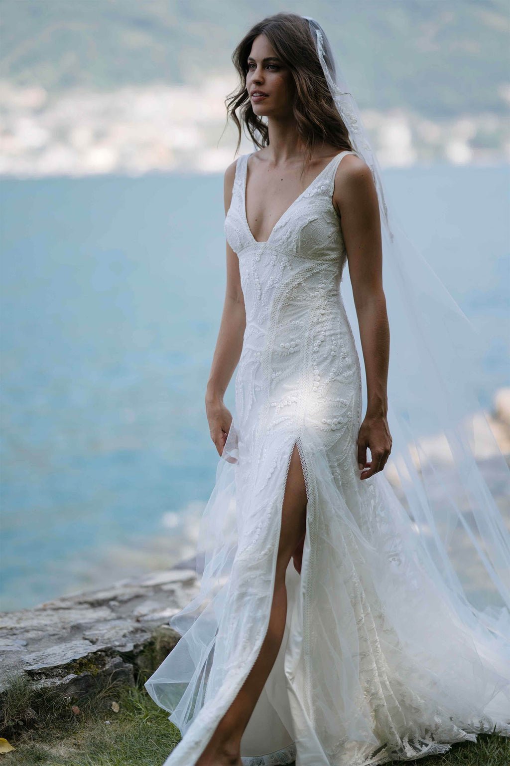 Model in Solstice gown and veil walking along grass with italian coastal line in background